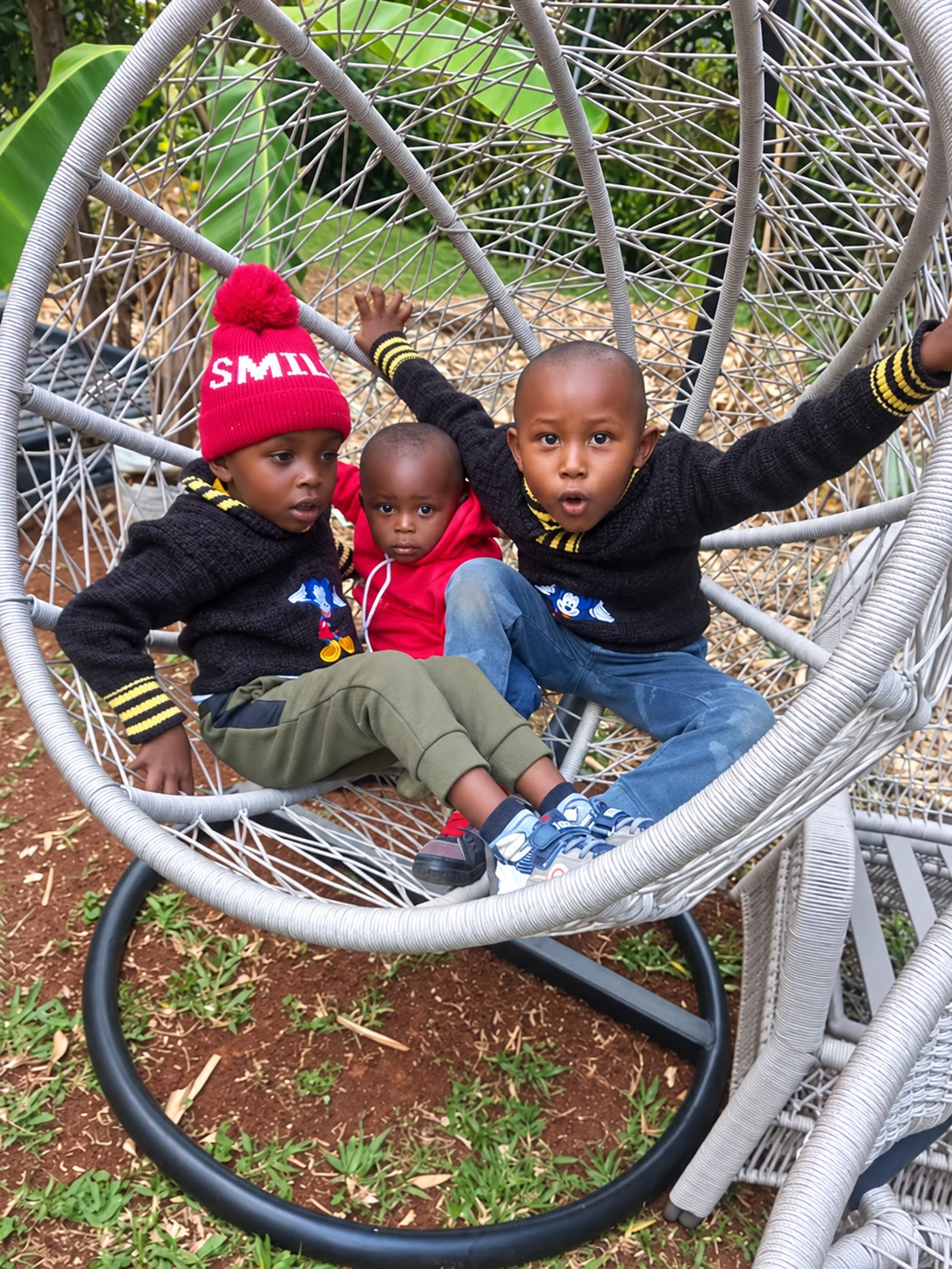 Three children sitting together in a woven outdoor chair